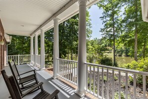 A covered porch with white columns and a white railing, overlooking a pond and trees. - Misty Lake Lodge, home on private lake (Westminster)