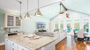 A spacious kitchen with a large island, pendant lights, and a dining area with a view of the outdoors.