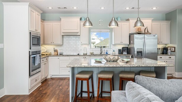 A modern kitchen with white cabinets, a central island with stools, stainless steel appliances, and pendant lighting.