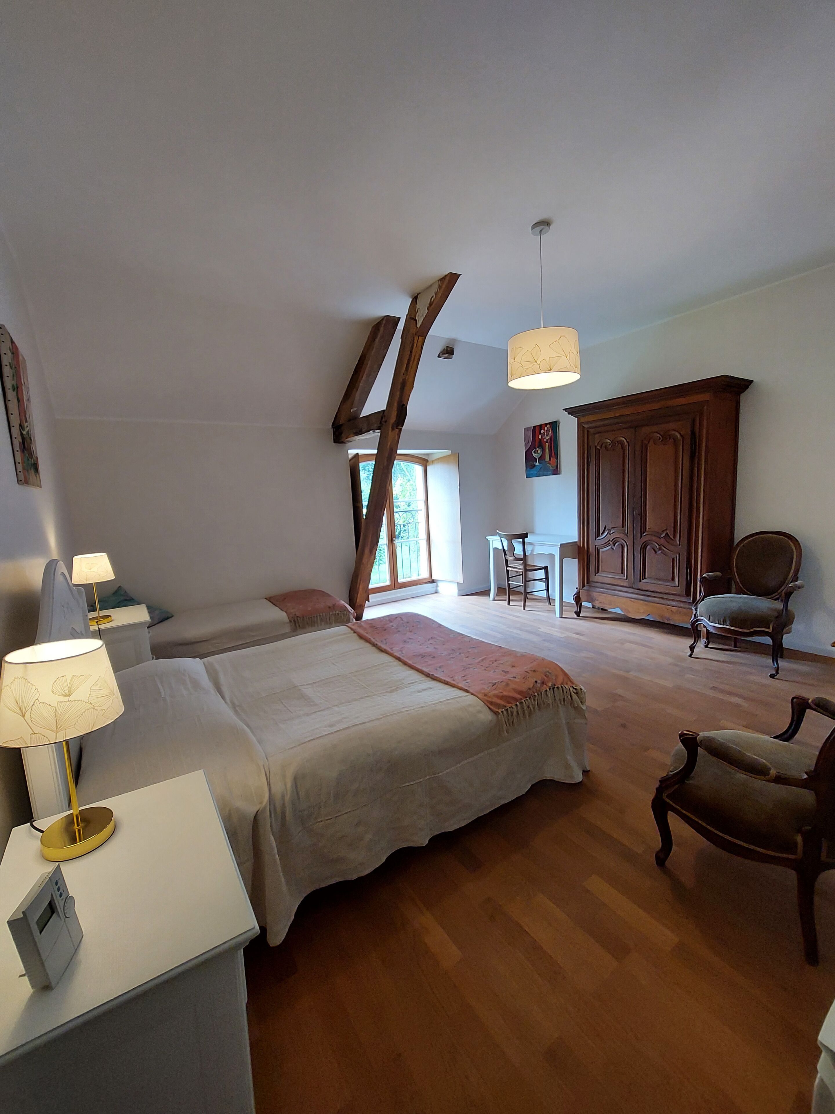A spacious bedroom with two beds, a wooden wardrobe, a desk with a lamp, and a chair.