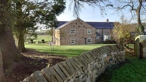 Traditional stone house with a central entrance and flanked windows, set amidst a well-maintained lawn and stone wall.