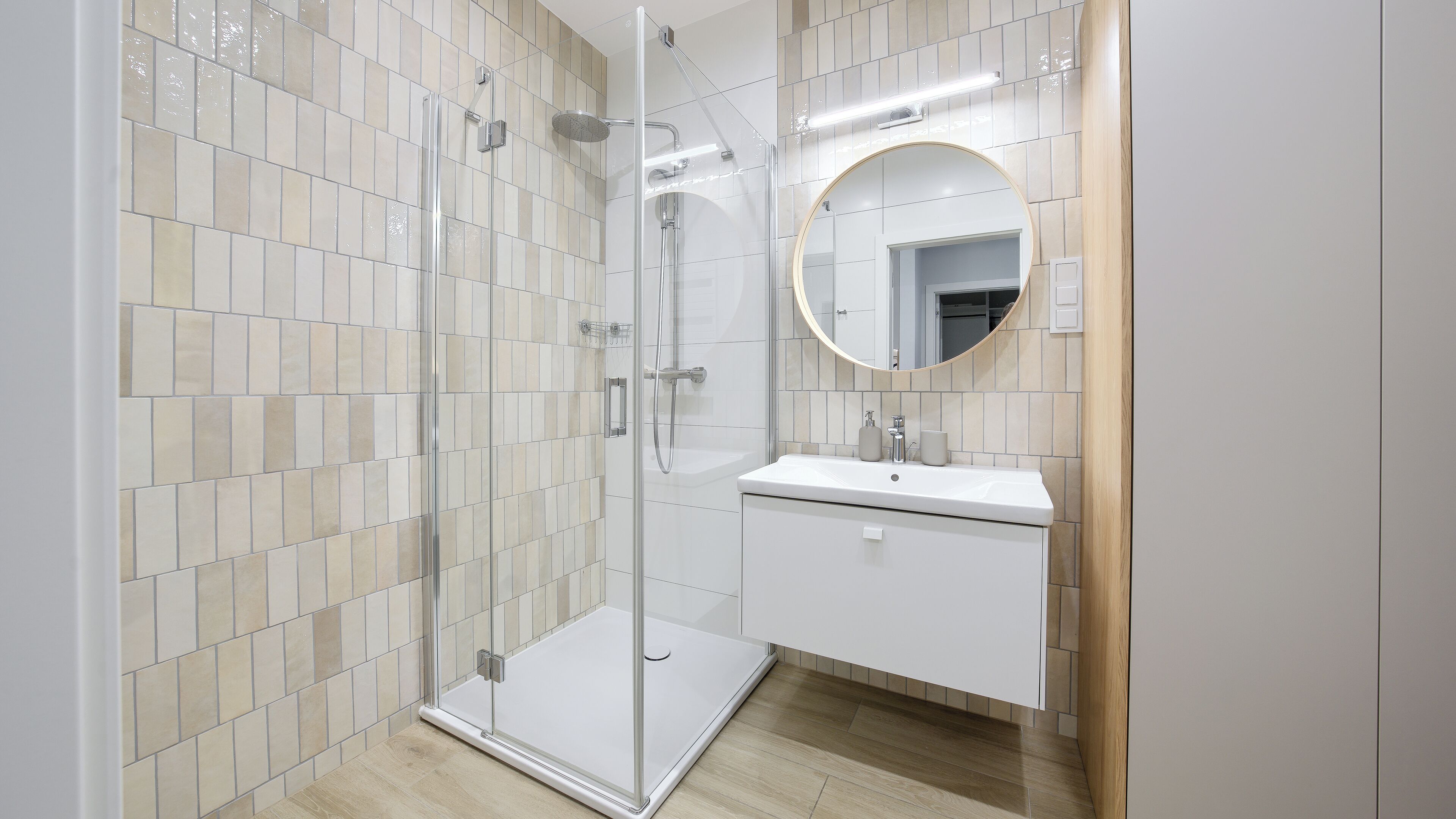 A modern bathroom with a glass-enclosed shower, a round mirror, and a white vanity.