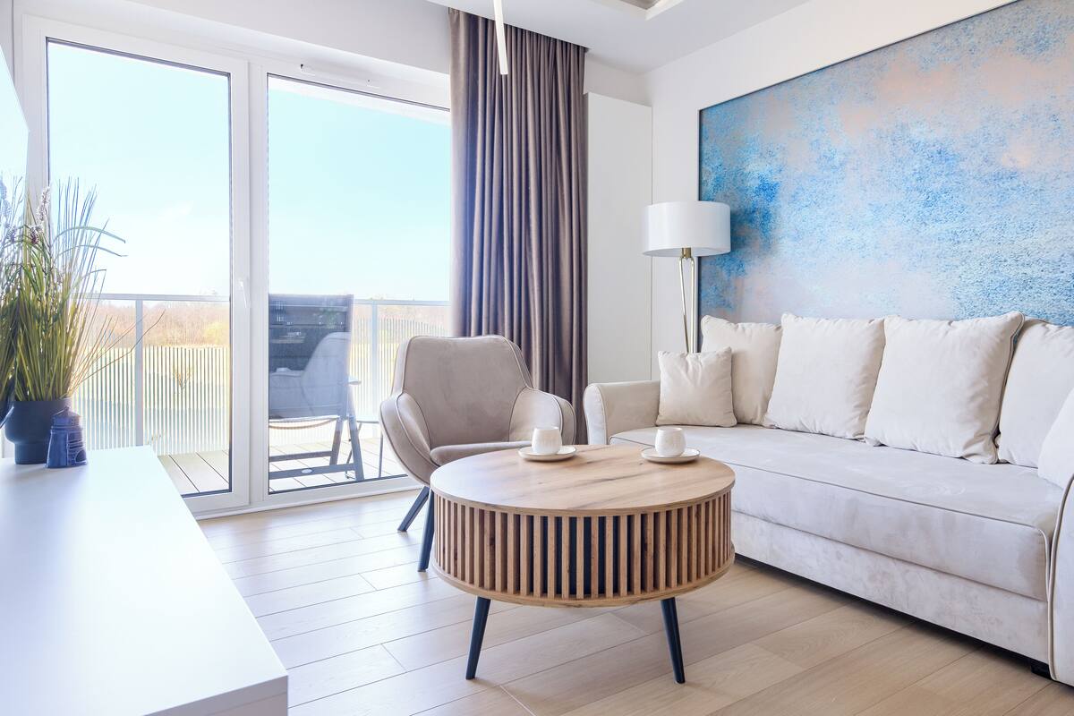 Una sala de estar moderna con un sofá, dos sillones, una mesa de centro redonda de madera, una lámpara de pie y un cuadro abstracto grande en la pared.