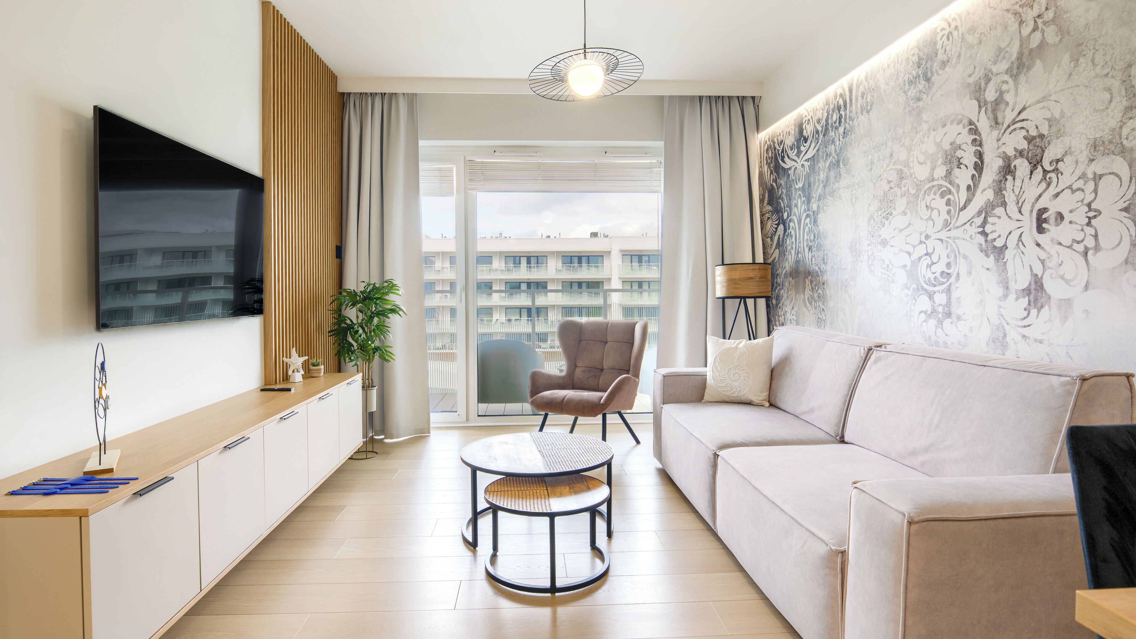 A modern living room with a sofa, a chair, a coffee table, a TV, and a large window with a view of buildings.