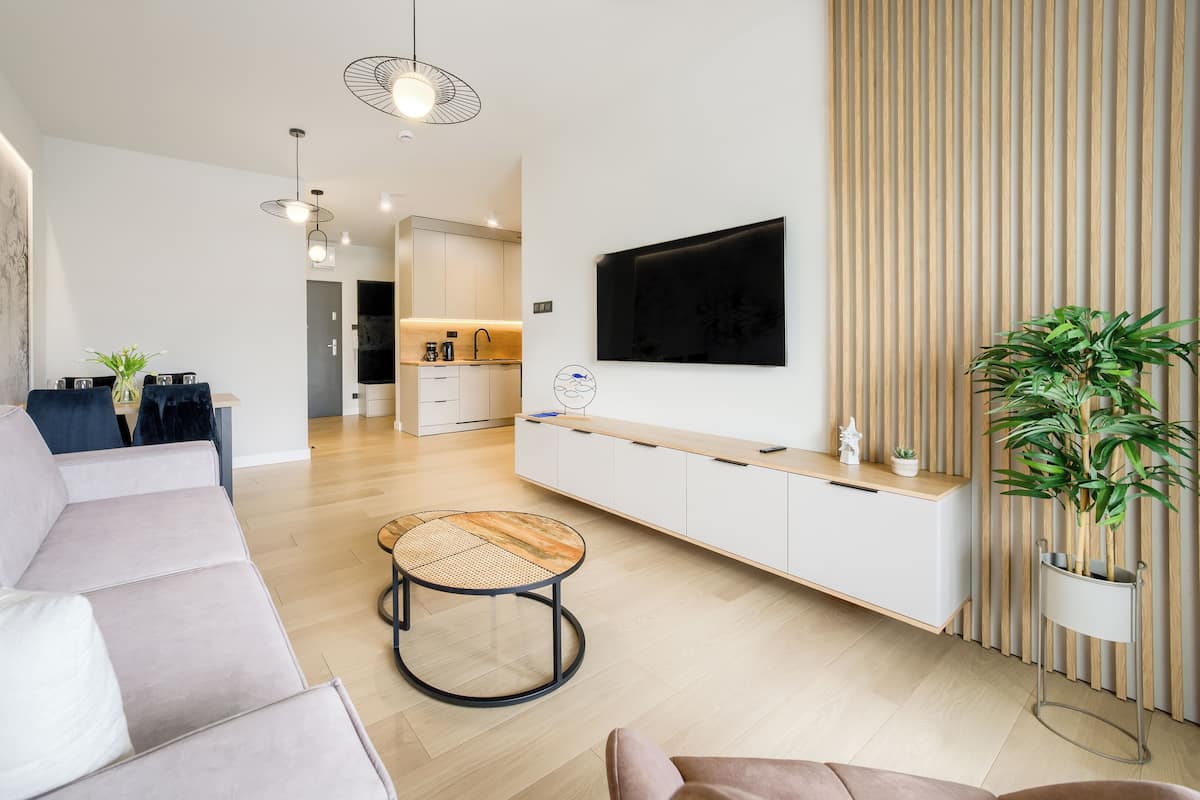 Una sala de estar moderna con sofá, mesa de centro, televisor montado en la pared y cocina al fondo.