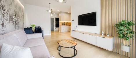 Una sala de estar moderna con sofá, mesa de centro, televisor montado en la pared y cocina al fondo.