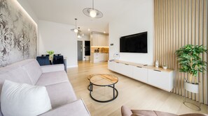 Una sala de estar moderna con sofá, mesa de centro, televisor montado en la pared y cocina al fondo.