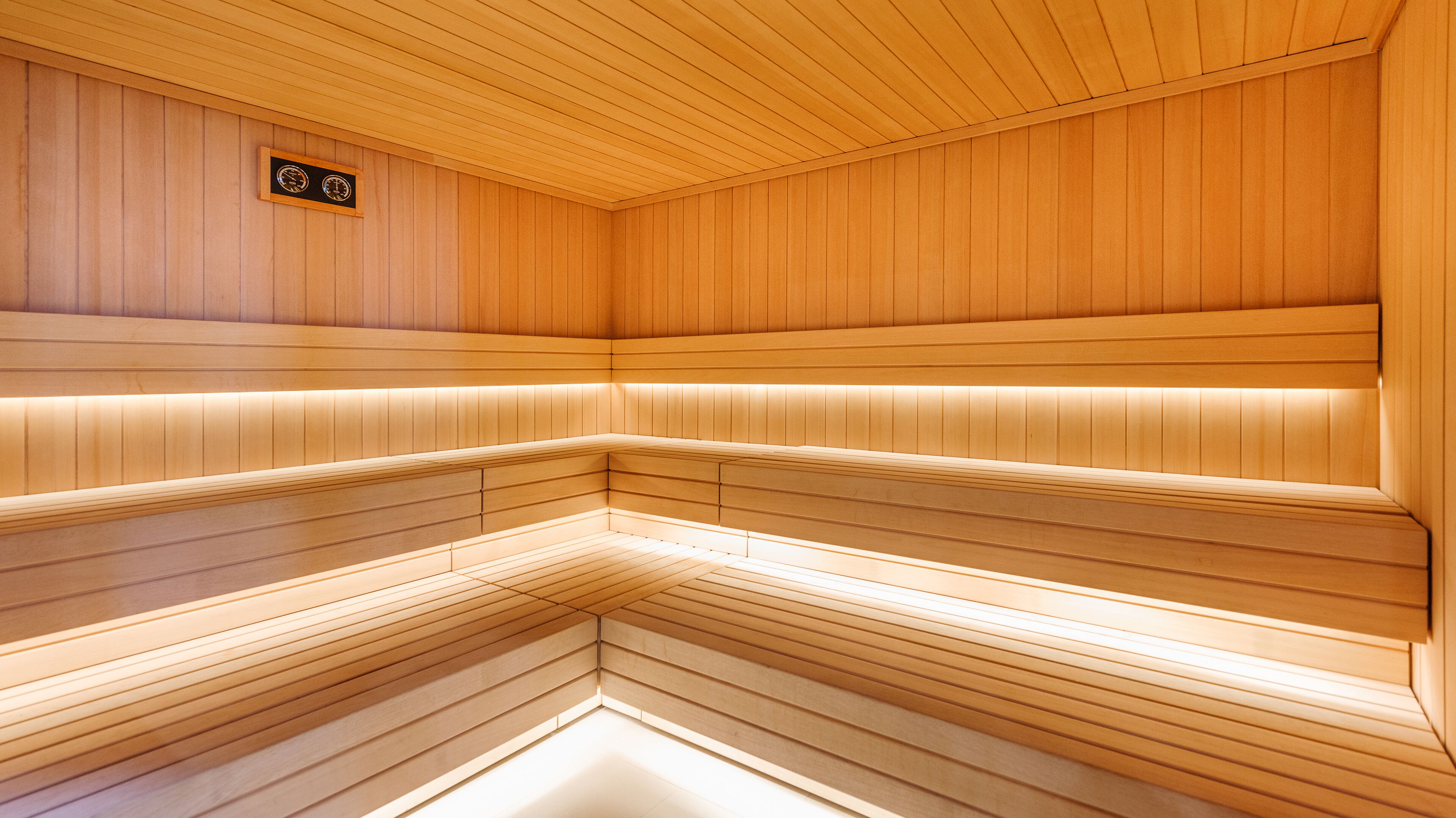 A sauna with wooden walls and benches, a clock, and a sign indicating the temperature.