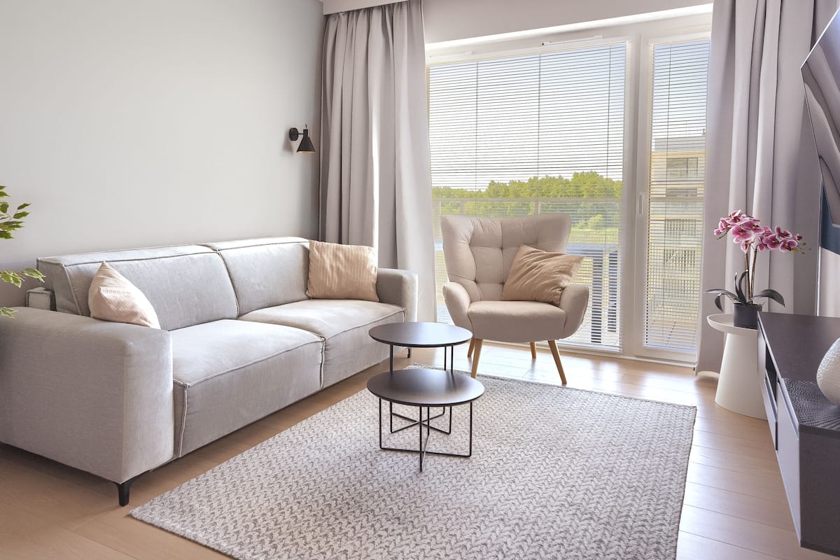 Una sala moderna con un sofá gris, una mesa redonda de centro, una mesita auxiliar, una planta en maceta y una silla.