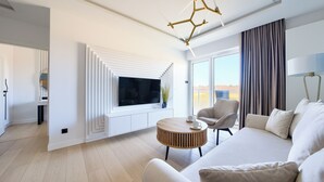 A modern living room with a flat-screen TV, a round wooden coffee table, a sofa, and a chair. - Apartamenty Sun & Snow Polanki Aqua (Kolobrzeg)