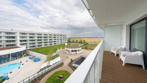 Un balcón con sillas blancas, una piscina y un edificio con múltiples balcones al fondo.