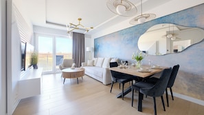 En moderne stue med spiseplads, sofa, sofabord og et stort vindue.