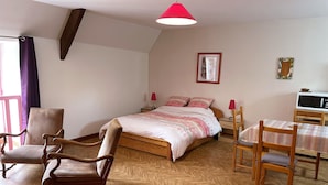 Quarto com uma cama, duas cadeiras, uma mesa, um micro-ondas e um abajur vermelho.
