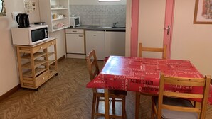Uma cozinha compacta com micro-ondas, torradeira e pia. Há uma mesa de jantar com cadeiras e toalha de mesa vermelha.