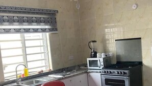 A kitchen with a sink, a microwave, a stove, and a red bar counter with chairs. - Immaculate 2-bed Apartment in Lekki Ajah (Lekki)