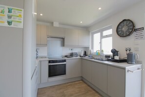 A modern kitchen with white cabinets, a built-in oven, a sink, and a clock on the wall.