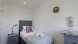 Une chambre à coucher comprenant un lit, une table de chevet, une lampe, une serviette, une figurine de cheval de mer décorative et une étagère fixée au mur.