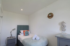 A bedroom with a bed, a bedside table, a lamp, a towel, a decorative seahorse, and a wall-mounted shelf.