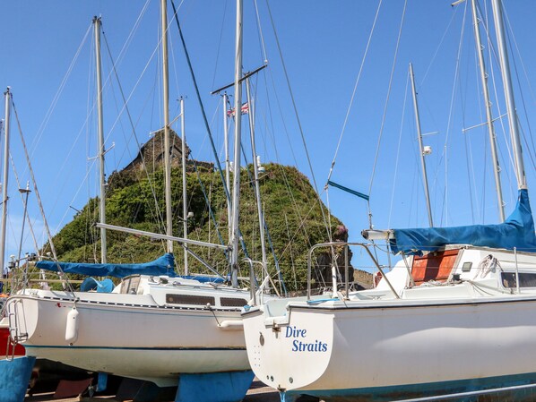 Un puerto deportivo con varios veleros amarrados, una isla destacada al fondo y un edificio con fachada de piedra.