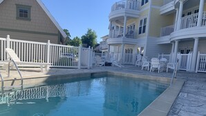 A swimming pool with a white fence, lounge chairs, and a building with balconies.
