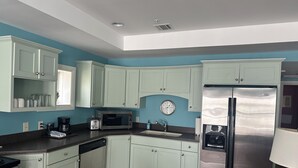 A kitchen with light green cabinets, a stainless steel refrigerator, a microwave, and a clock on the wall.