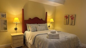 A neatly made bed with a wooden headboard, two bedside lamps, a nightstand, and a dresser.