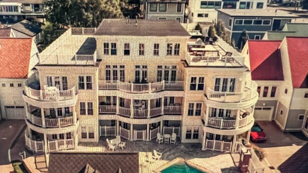 A multi-story building with balconies, a swimming pool, and a red-roofed structure nearby.