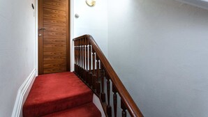 Eine Holztreppe mit rotem Teppich, weißen Wänden und einer Holztür.