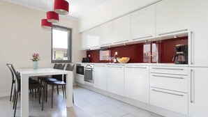 A modern kitchen with white cabinets, a dining table with chairs, and red pendant lights. - Elite Apartments Szafarnia King Size (Gdansk)
