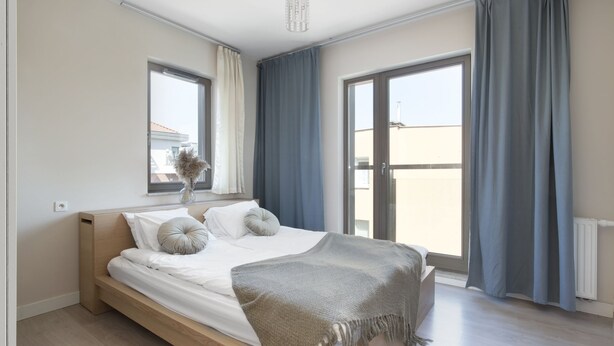 A modern bedroom with a wooden bed, a large window, and a view of the outside. - Elite Apartments Szafarnia King Size (Gdansk)