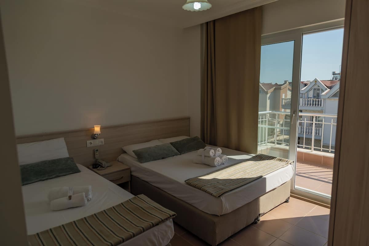 A hotel room with two beds, a balcony with a view of buildings, and a sliding glass door.