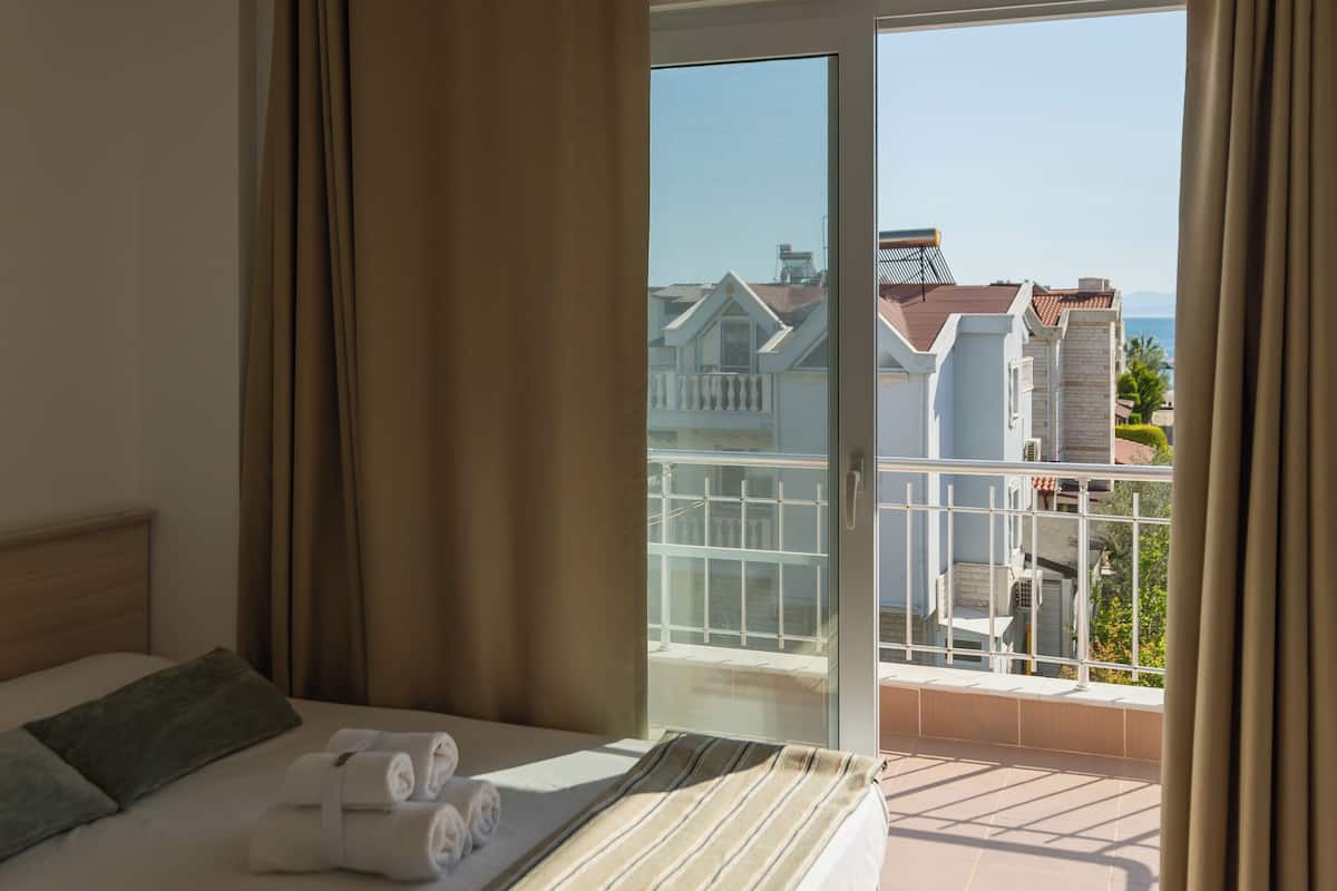 A hotel room with a bed, a balcony with a view of buildings, and a hanging light fixture.