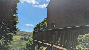 Una terraza de madera con vista a un paisaje verde y un edificio de ladrillo.