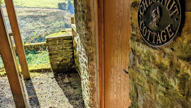 Una rústica puerta de madera con un muro de piedra y una placa de metal que dice "Chestnut Cottage".