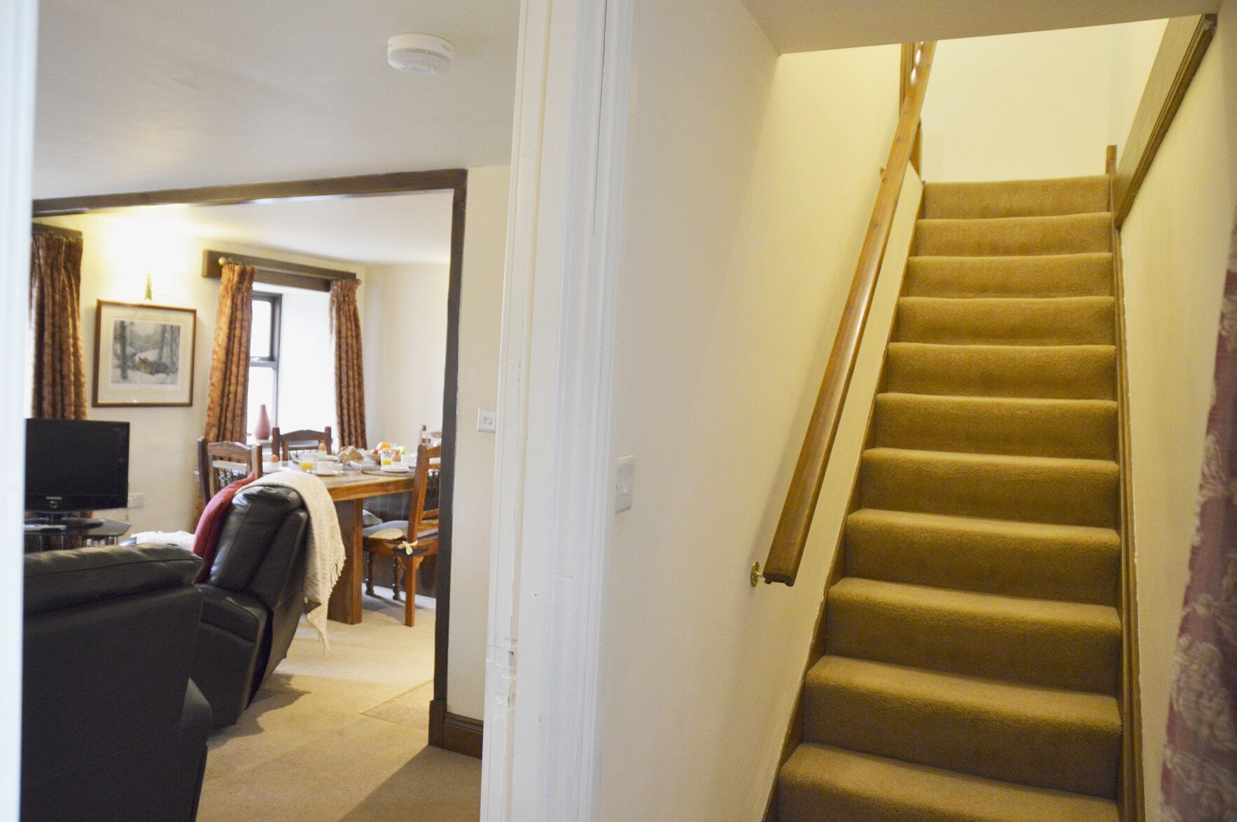 A staircase with carpeted steps and a wooden handrail, leading to a dining area with a table and chairs.