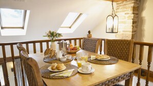 A dining table set with breakfast items, including croissants, bread, and fruit, in a room with wooden chairs and a stone wall. - Bothy (Alston)