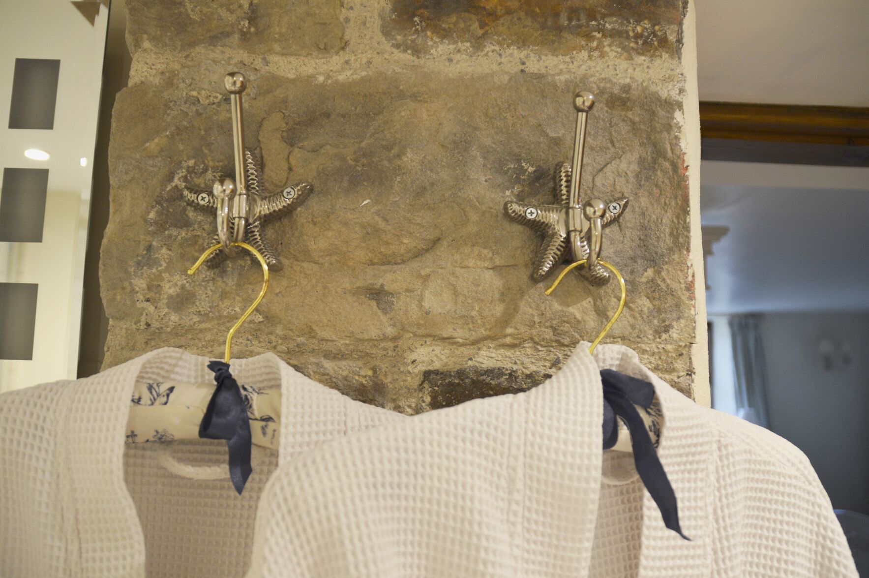 A pair of white sweaters with dark ribbons hanging on a wall-mounted hook.