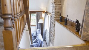 A narrow staircase with a wooden handrail, a stone wall, and a window with curtains. - Bothy (Alston)