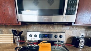 A kitchen with a stainless steel microwave, a stove with pots, a toaster, and wooden cabinets. - String light condo with chic brick interior (Midland)