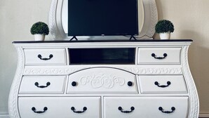 A white dresser with a television on top, two small potted plants, and a ceiling fan. - String light condo with chic brick interior (Midland)