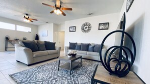 A modern living room with two sofas, a coffee table, and decorative items. There are ceiling fans, a clock, and framed pictures on the wall. - String light condo with chic brick interior (Midland)