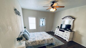 A bedroom with a bed, dresser, ceiling fan, and two windows. - String light condo with chic brick interior (Midland)