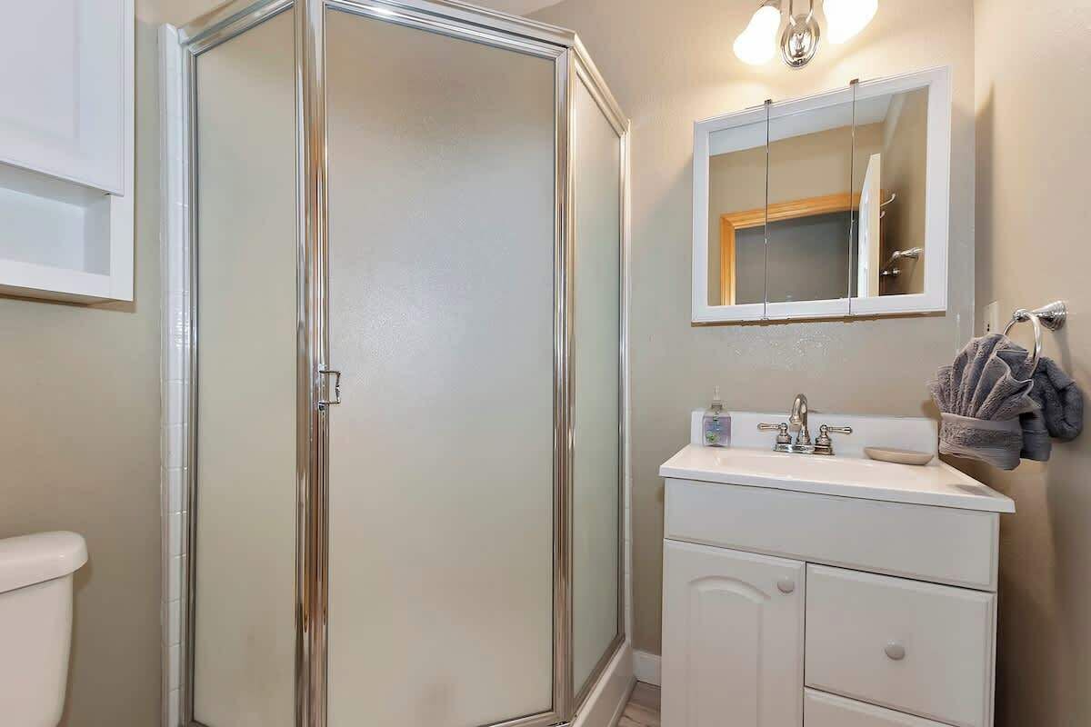 Une salle de bain avec une douche à parois de verre, un lavabo blanc avec un miroir au-dessus et un porte-serviettes avec des serviettes.