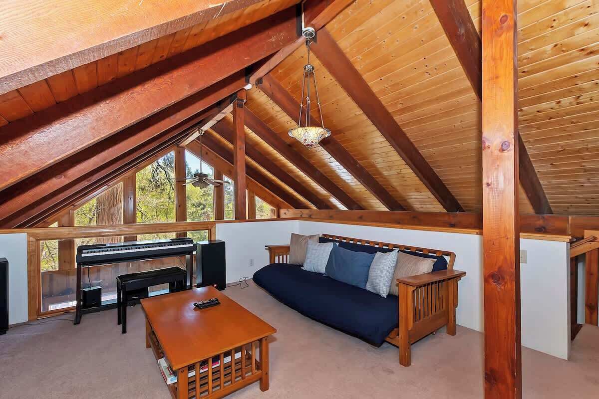 Une pièce mansardée chaleureuse avec un plafond en bois, un canapé, une table et un piano.