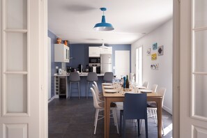 Une cuisine moderne avec des meubles blancs, une table à manger pour quatre personnes et un luminaire suspendu bleu.
