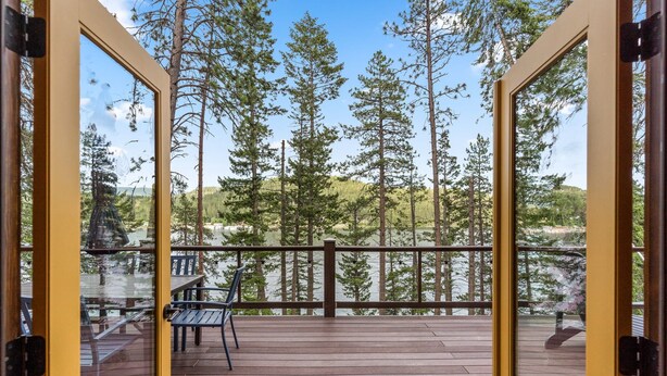 Une terrasse en bois ouverte, offrant une vue sur de grands pins et un lac.
