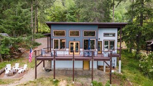 Une cabane à deux étages avec une terrasse, entourée de forêt.