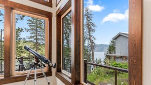 Une pièce dotée de grandes fenêtres donnant sur une forêt et un lac. Un télescope est installé sur un trépied près des fenêtres.