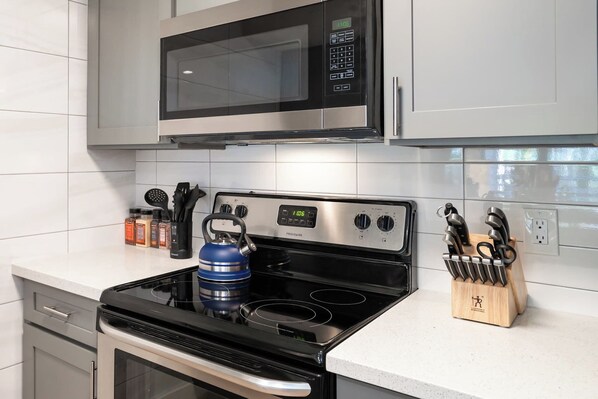 Una cocina con microondas de acero inoxidable, estufa negra y bloque de cuchillos.