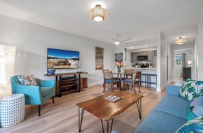 Un salon avec une table basse en bois, des canapés bleus et un coin repas comprenant des chaises et un téléviseur.